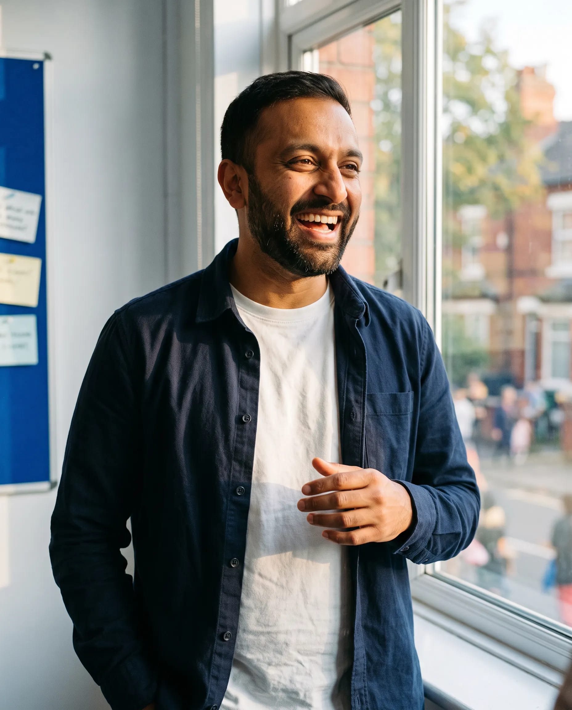 Rayhan Ahmed, youth mentor, in a warmer portrait by the window of the community space in Levenshulme, Manchester